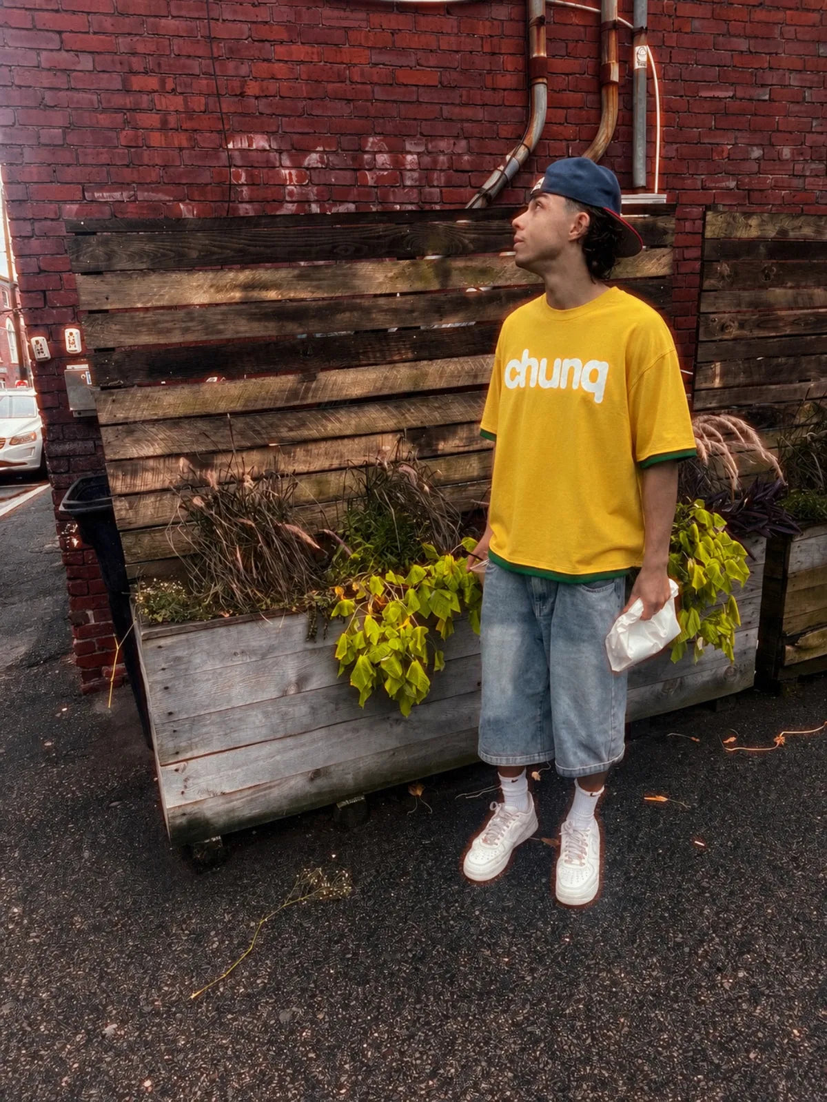 Model wearing a yellow Chunq jersey beside a brick wall