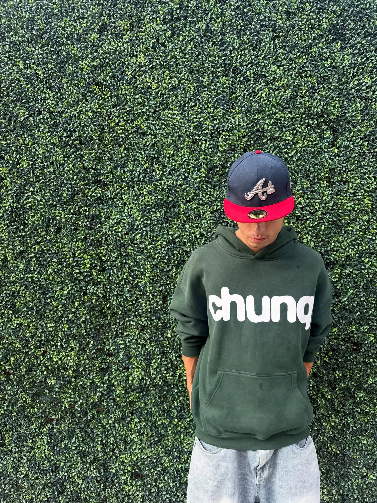 Model wearing a green Chunq hoodie against a hedge