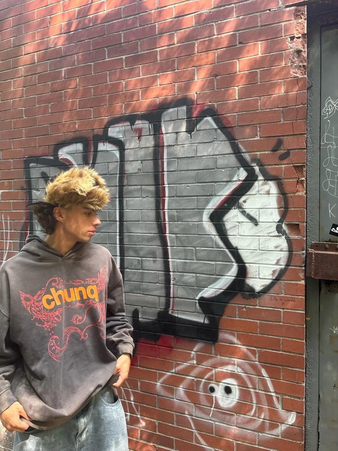 Model wearing a brown graphic Chunq hoodie against a brick wall