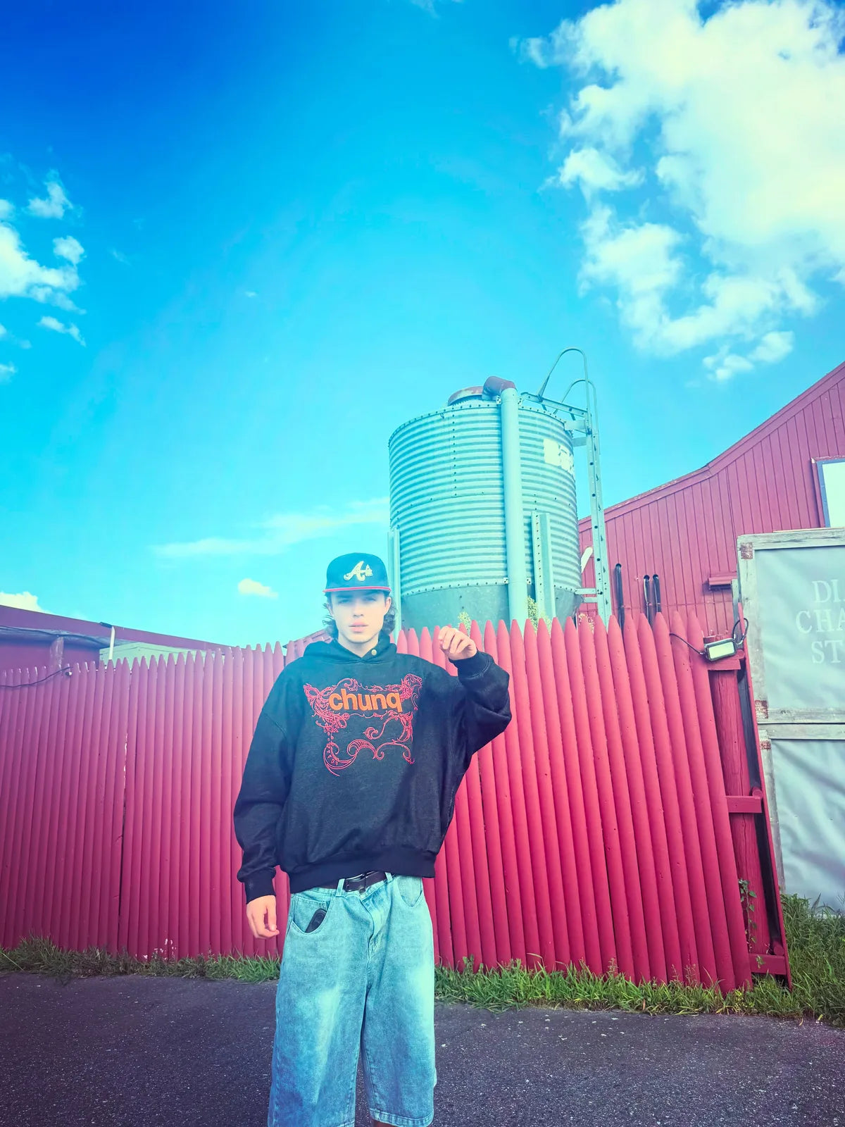 Model wearing a brown graphic Chunq hoodie beside a red building